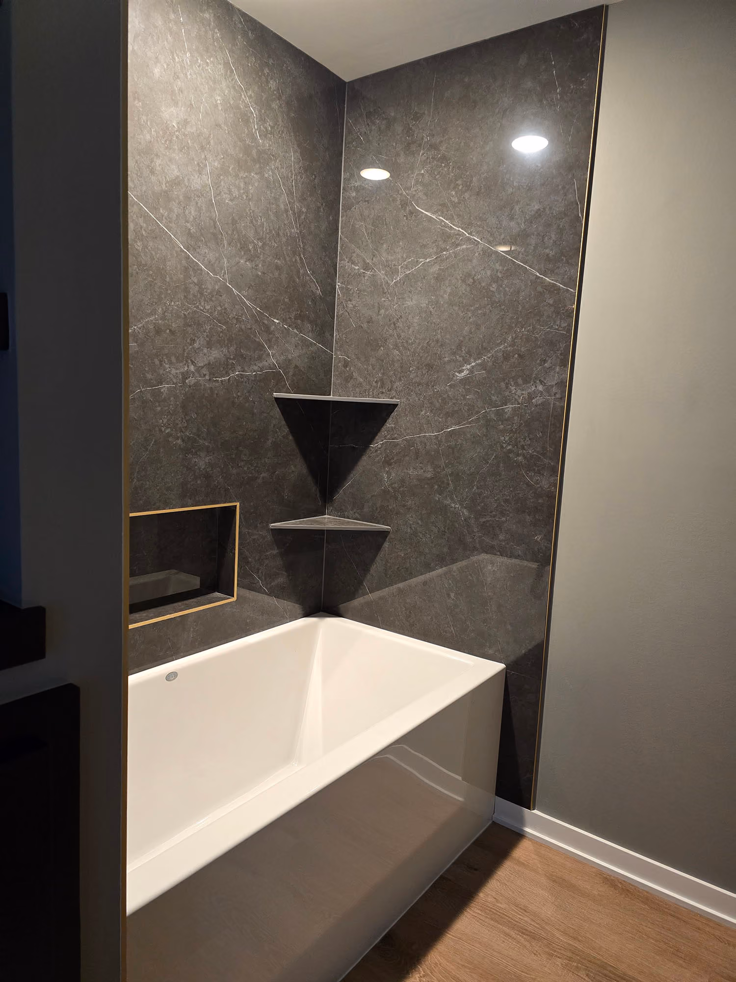Bathtub with dark tiled shower and glass panel