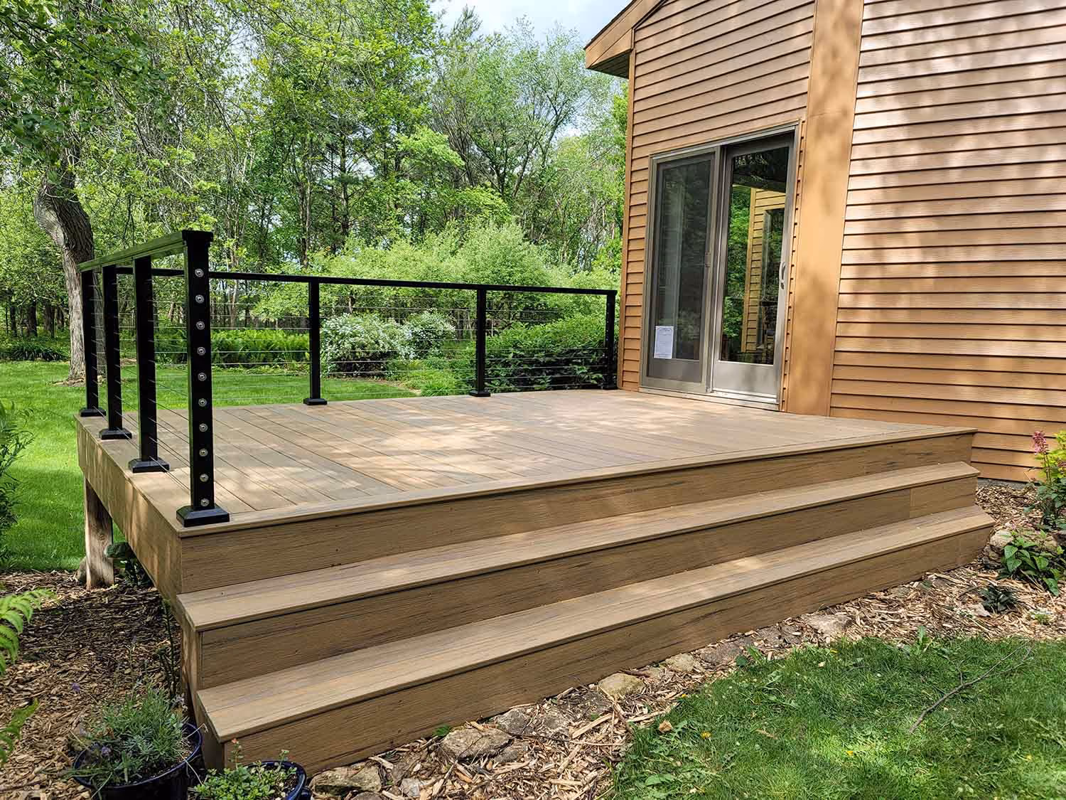 Ground-level deck with steps and black railing in wooded yard