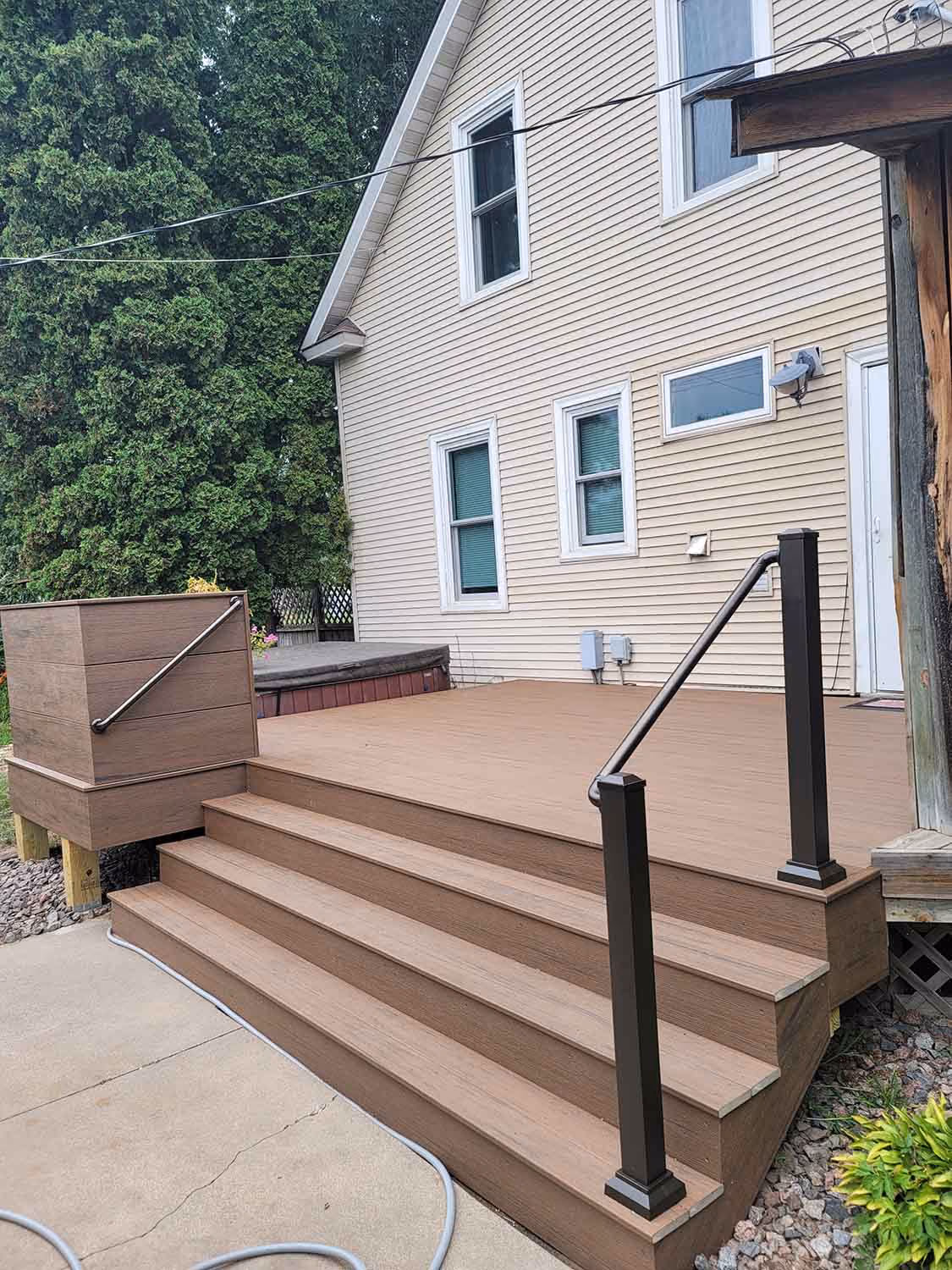 Wooden deck stairs with black handrail beside house