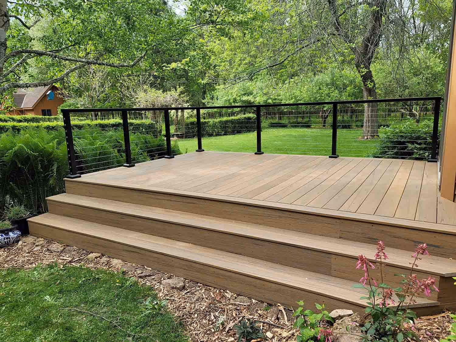 Curved wooden deck platform with black railing in backyard