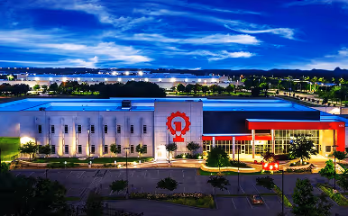 Aerial view of a modern building illuminated at night with a red and white exterior, set against a cityscape under a vivid blue sky.