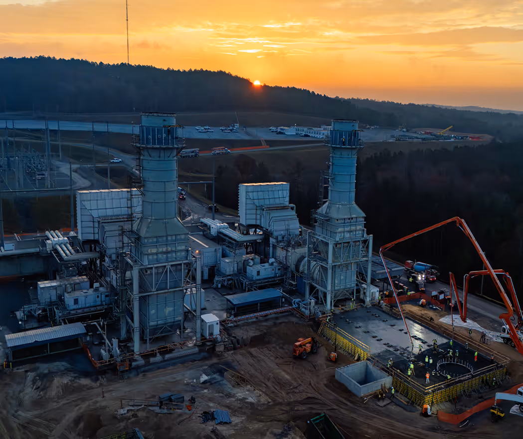 Industrial power plant with large machinery and workers on a construction site during sunset.