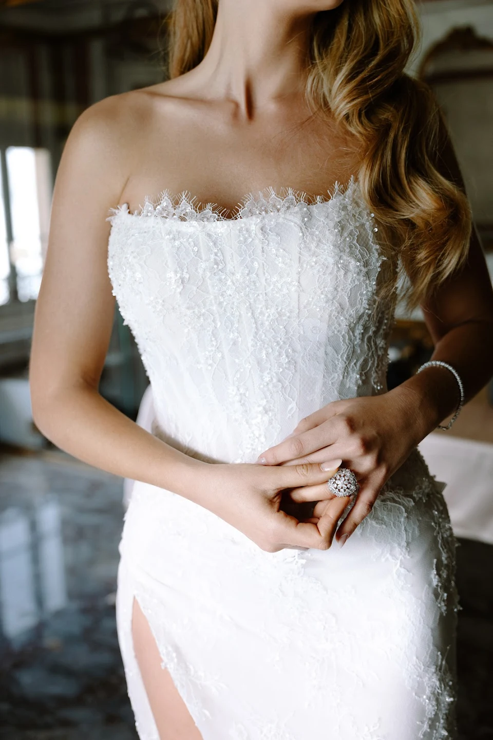 Close-up of a woman wearing a strapless white lace wedding dress with intricate beading, a large ring, and a bracelet.