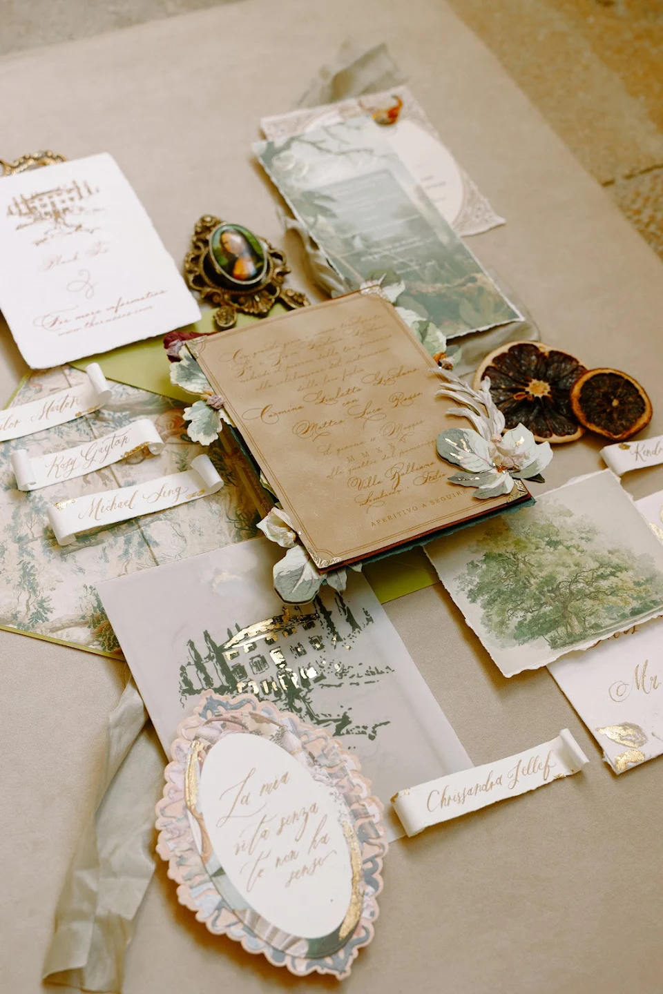 Vintage-style wedding invitation suite with handwritten calligraphy, decorative floral accents, dried orange slices, and watercolor illustrations.