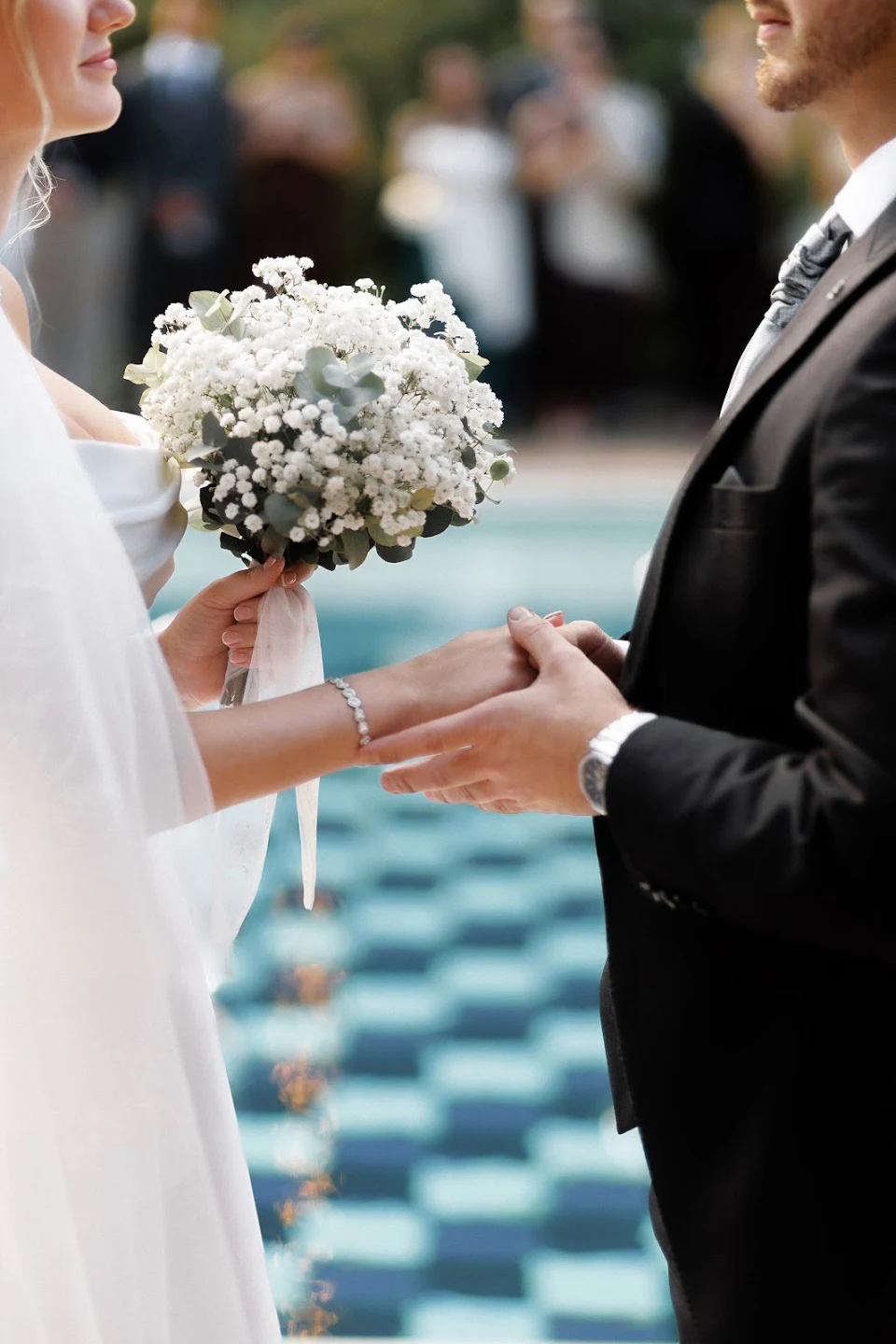 Bride and groom holding hands during a wedding ceremony, the bride holding a bouquet of white flowers.