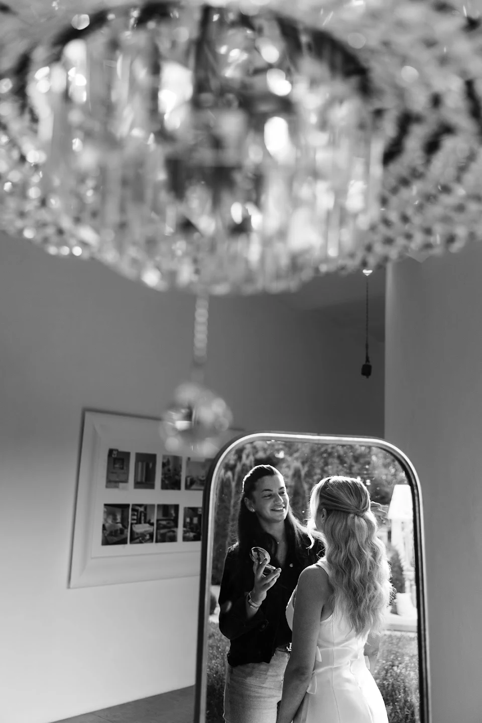 Black and white photo of a woman applying makeup on another woman in front of a mirror.