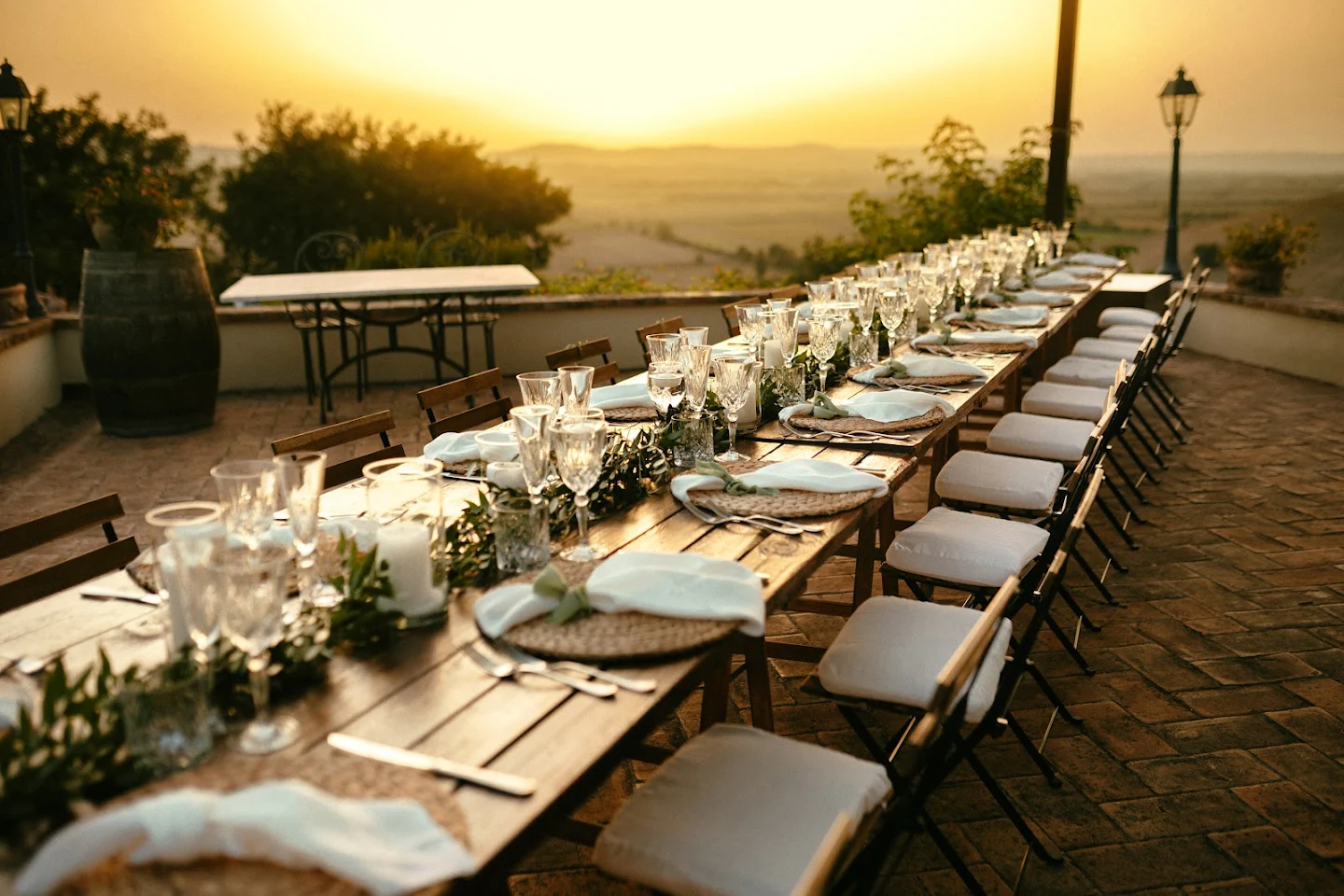 Long outdoor dining table set with glassware, cutlery, and napkins during sunset.