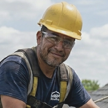 Smiling male construction worker wearing a yellow hard hat, safety glasses, and a harness outdoors.