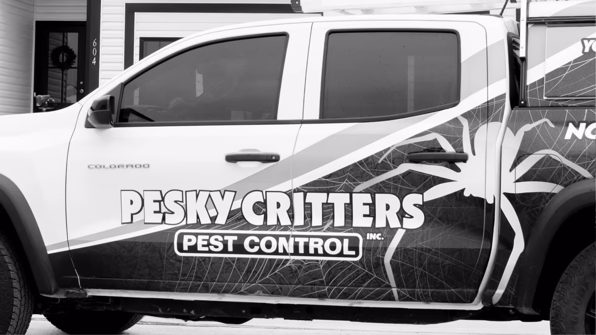Side view of a pickup truck with Pesky Critters Pest Control branding and a large spider graphic on the door.