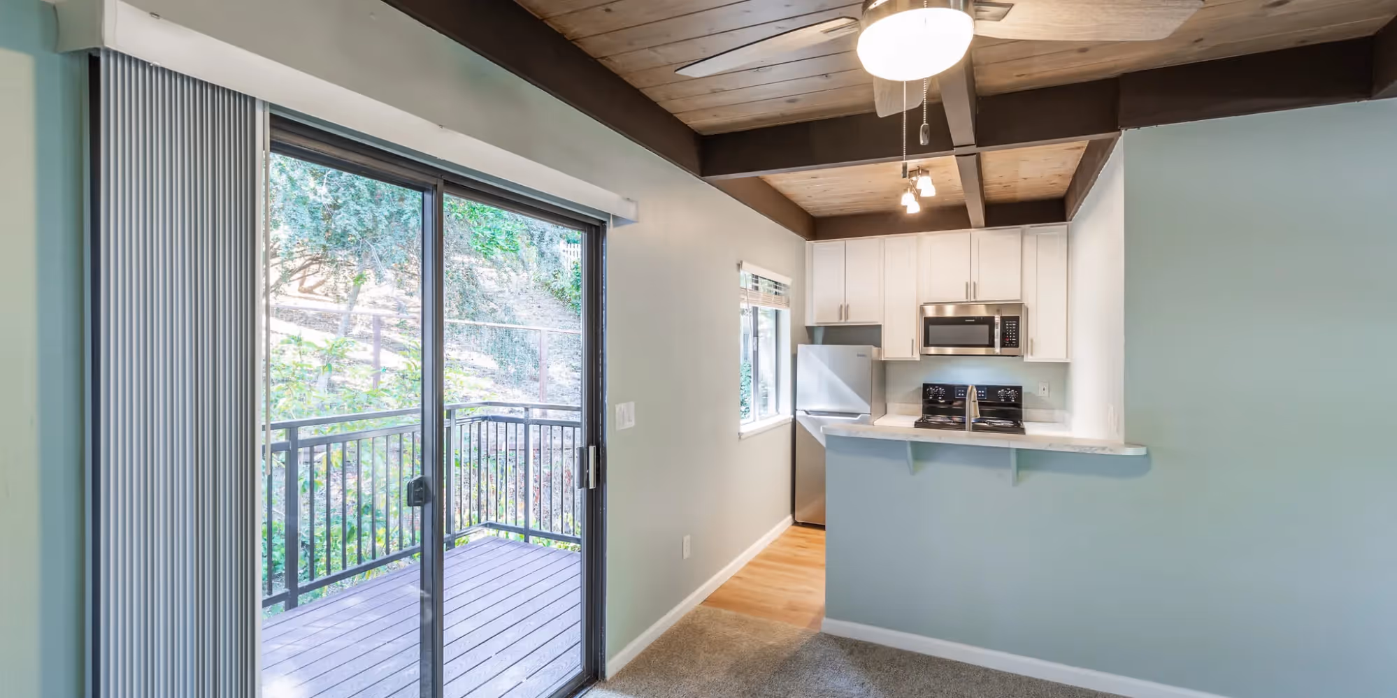 View of balcony doors and kitchen with breakfast bar, white cabinets, and stainless steel appliances