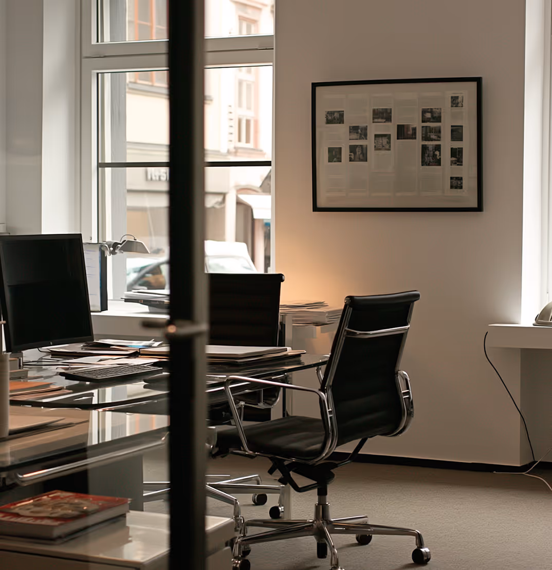 Modern office with black swivel chairs, a glass desk with papers and a computer, and a window showing a street view outside.