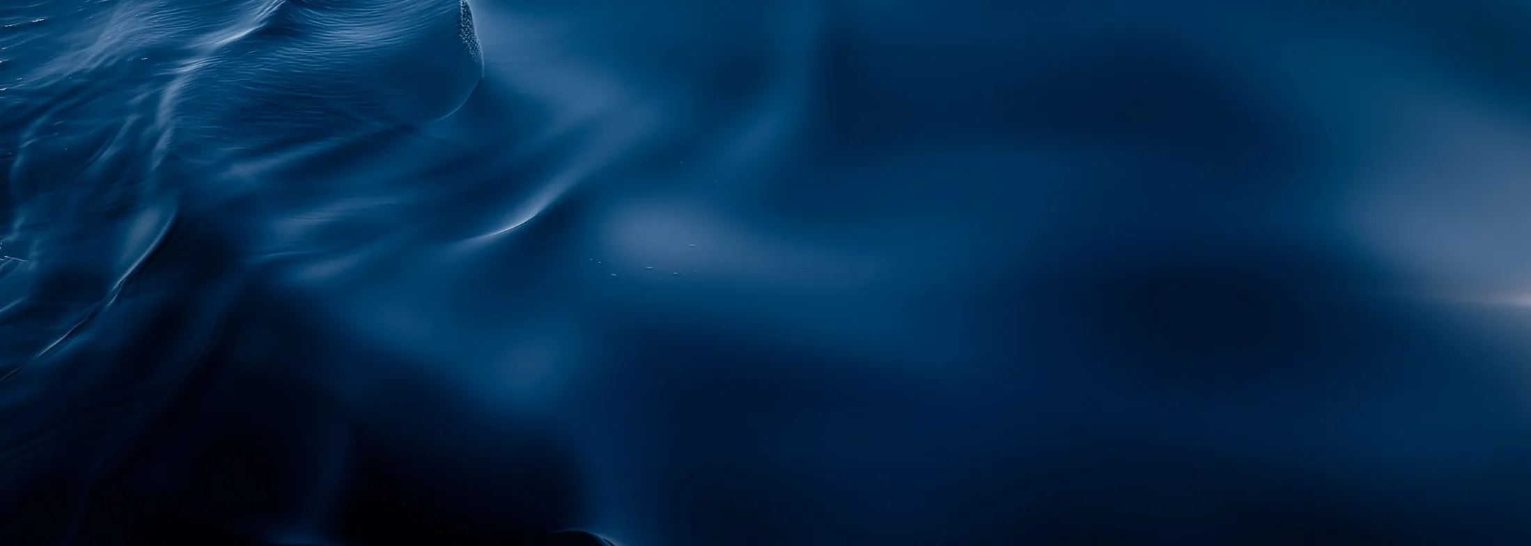 Close-up of smooth, dark blue water surface with gentle ripples and reflections.