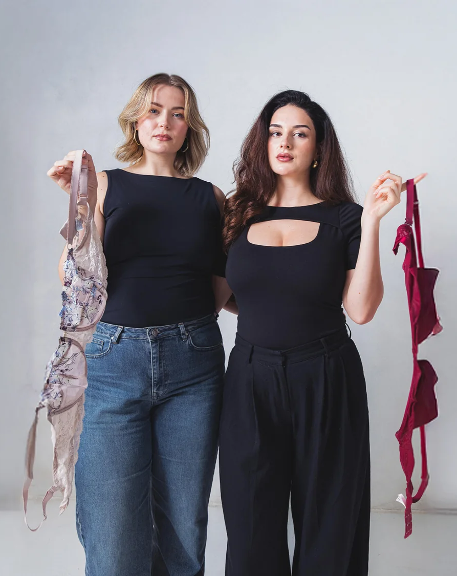 Close-up of a person wearing a white knit beanie, large black ski goggles, and a red winter jacket against a clear blue sky.