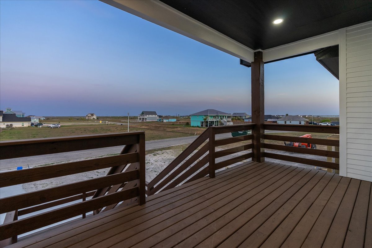 Empty wooden deck with railing overlooking a suburban area with houses and open land under a clear sky.
