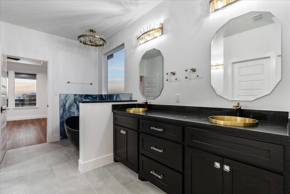 Modern bathroom with black double vanity, gold sinks, octagonal mirrors, and a black freestanding tub next to a blue marble accent wall.