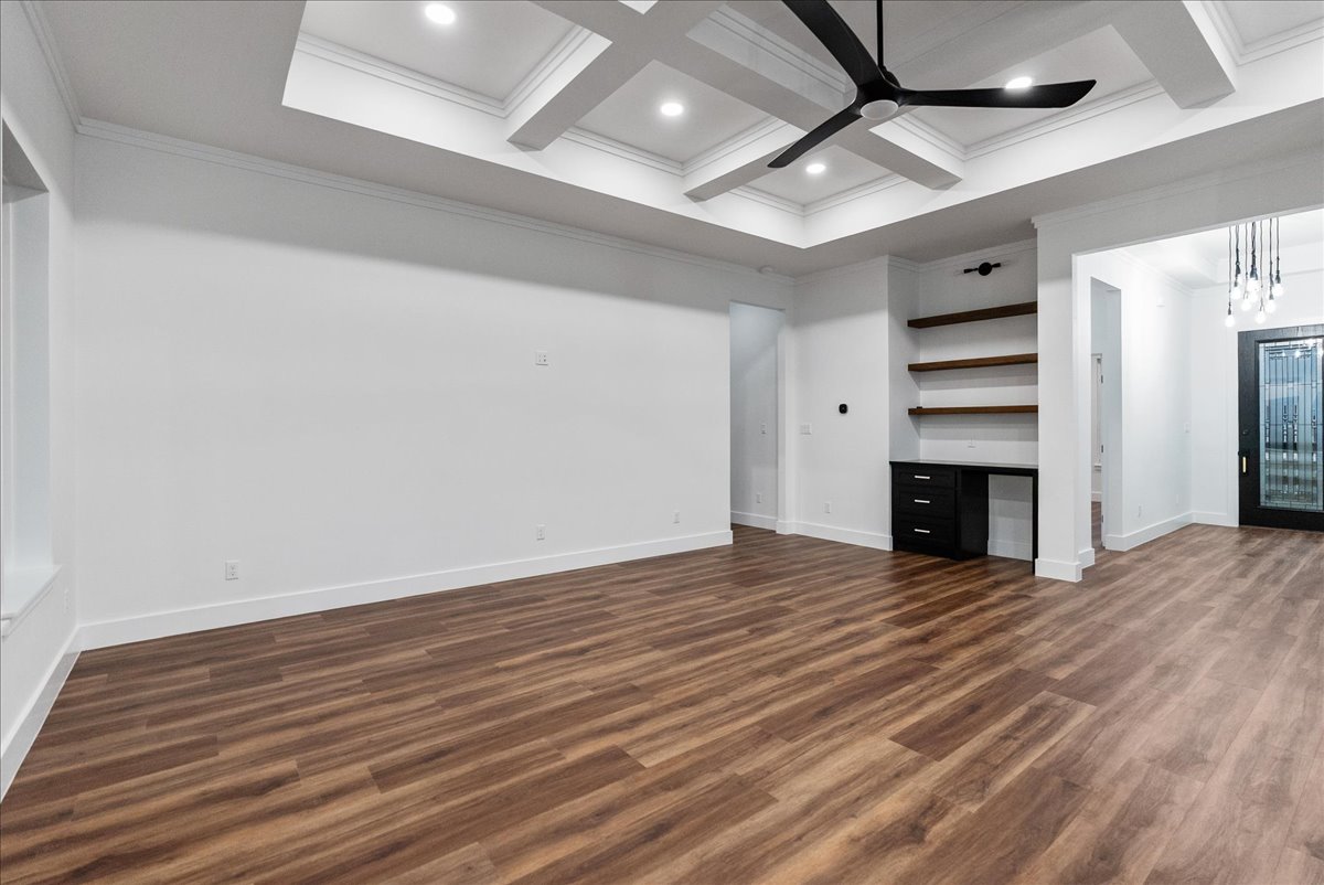 Empty modern room with wood flooring, white walls, recessed ceiling lights, a black ceiling fan, built-in shelves, and a black glass door.