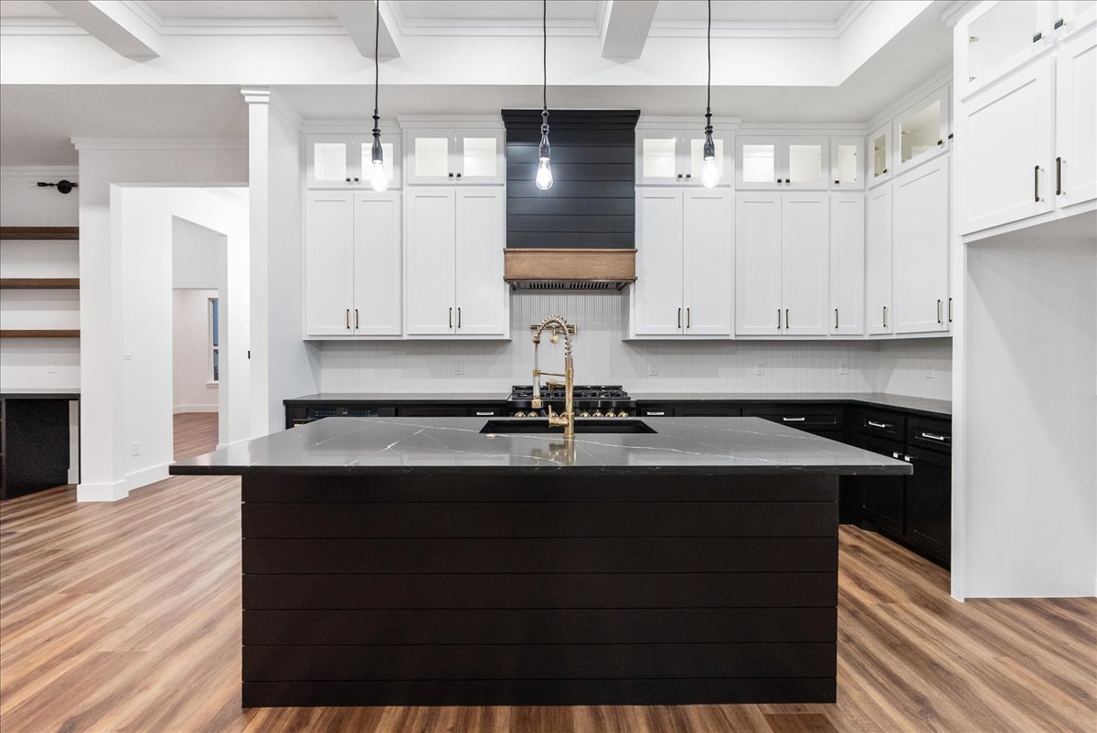 Modern kitchen with black island countertop, brass faucet, white upper cabinets, black lower cabinets, and wood flooring.