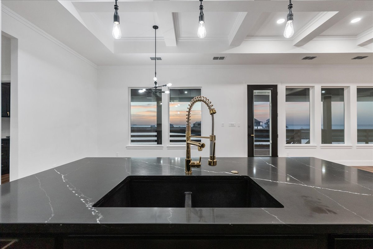 Modern kitchen island with black marble countertop and brass spring coil faucet, with large windows showing a sunset outside.