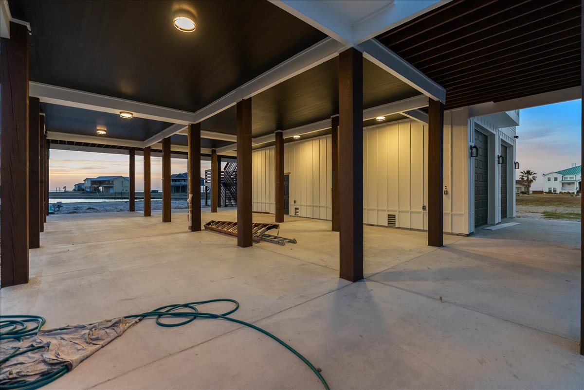 Covered concrete patio with wooden pillars and outdoor lighting at dusk, overlooking nearby houses and water.