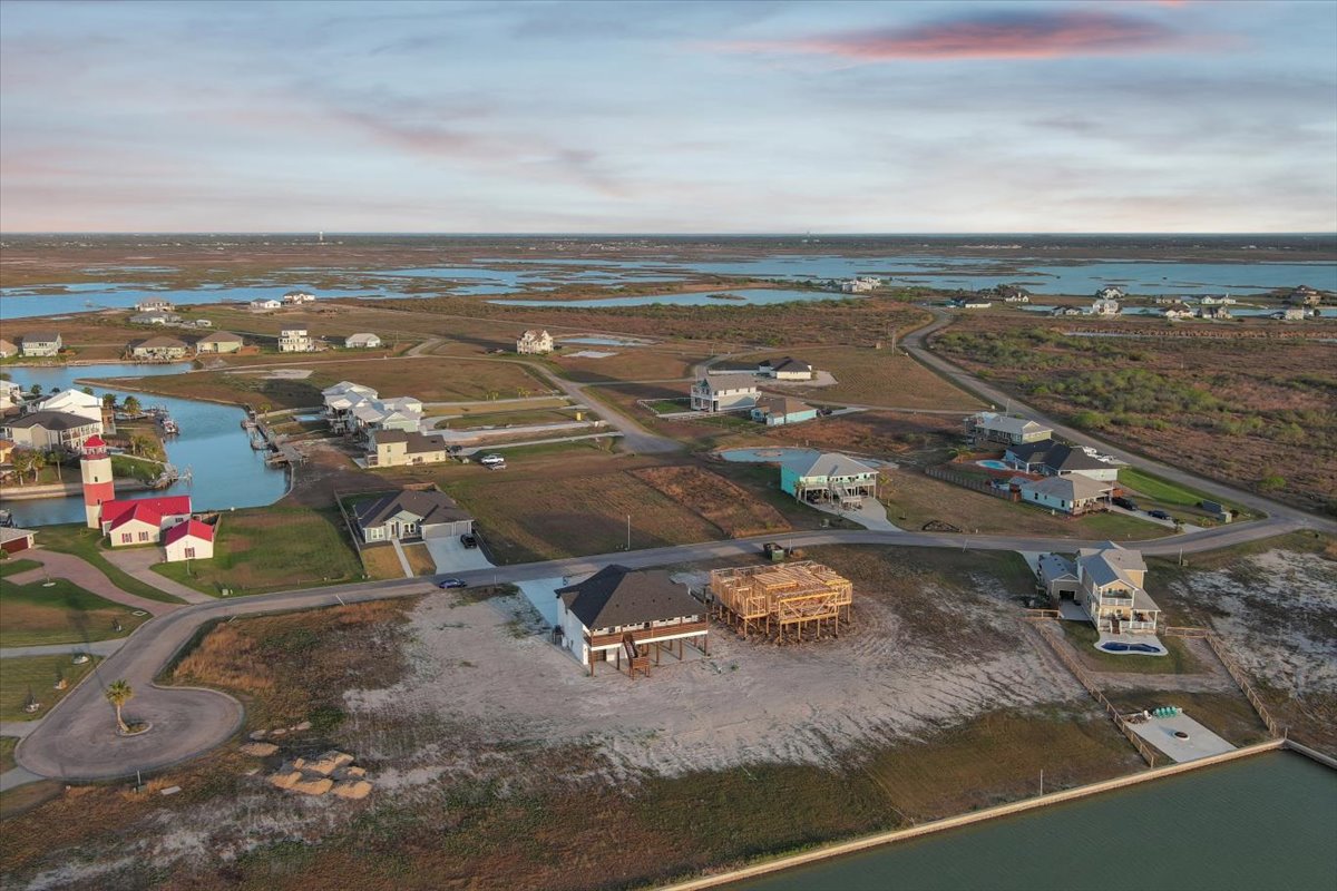 Aerial view of a coastal residential neighborhood with houses, a lighthouse, waterways, and marshland under a cloudy sky.
