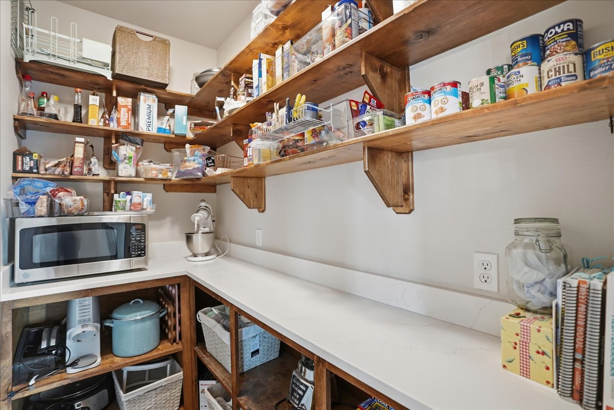 Well-organized pantry with wooden shelves holding canned goods, snacks, and kitchen appliances including a microwave and stand mixer.