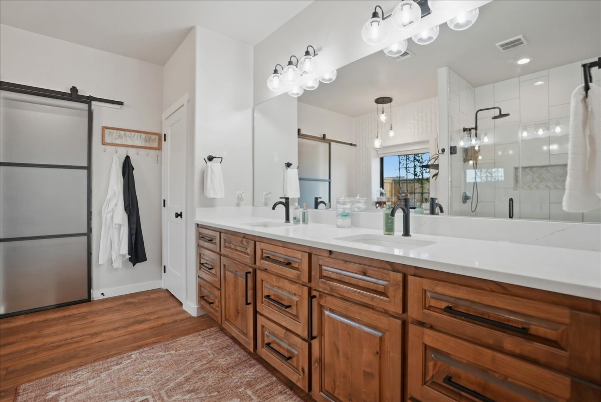 Modern bathroom with wooden double vanity, white countertop, black faucets, large mirror, and frosted sliding door.