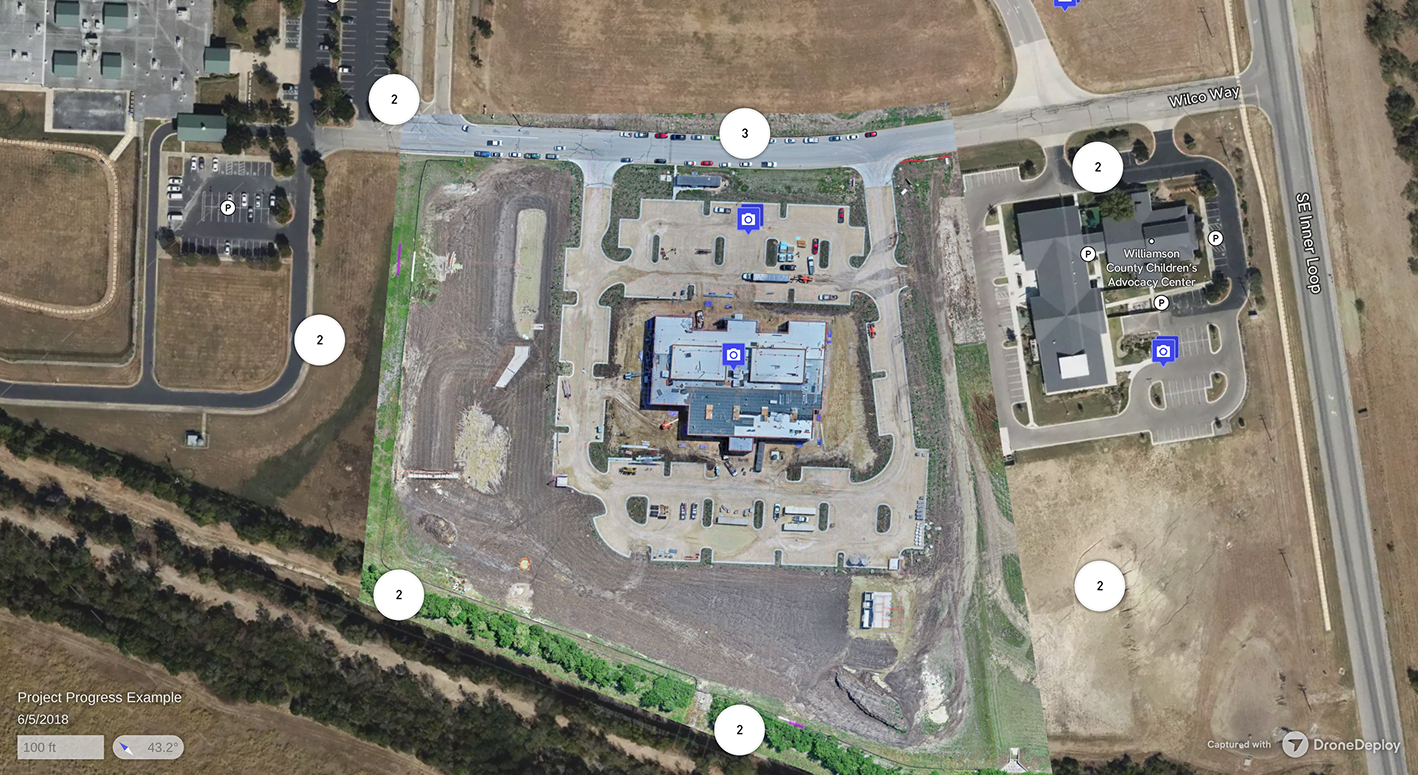 Aerial view of a construction site with a central building under construction, surrounding roads, parking lots, and adjacent Williamson County Children’s Advocacy Center building with parking.