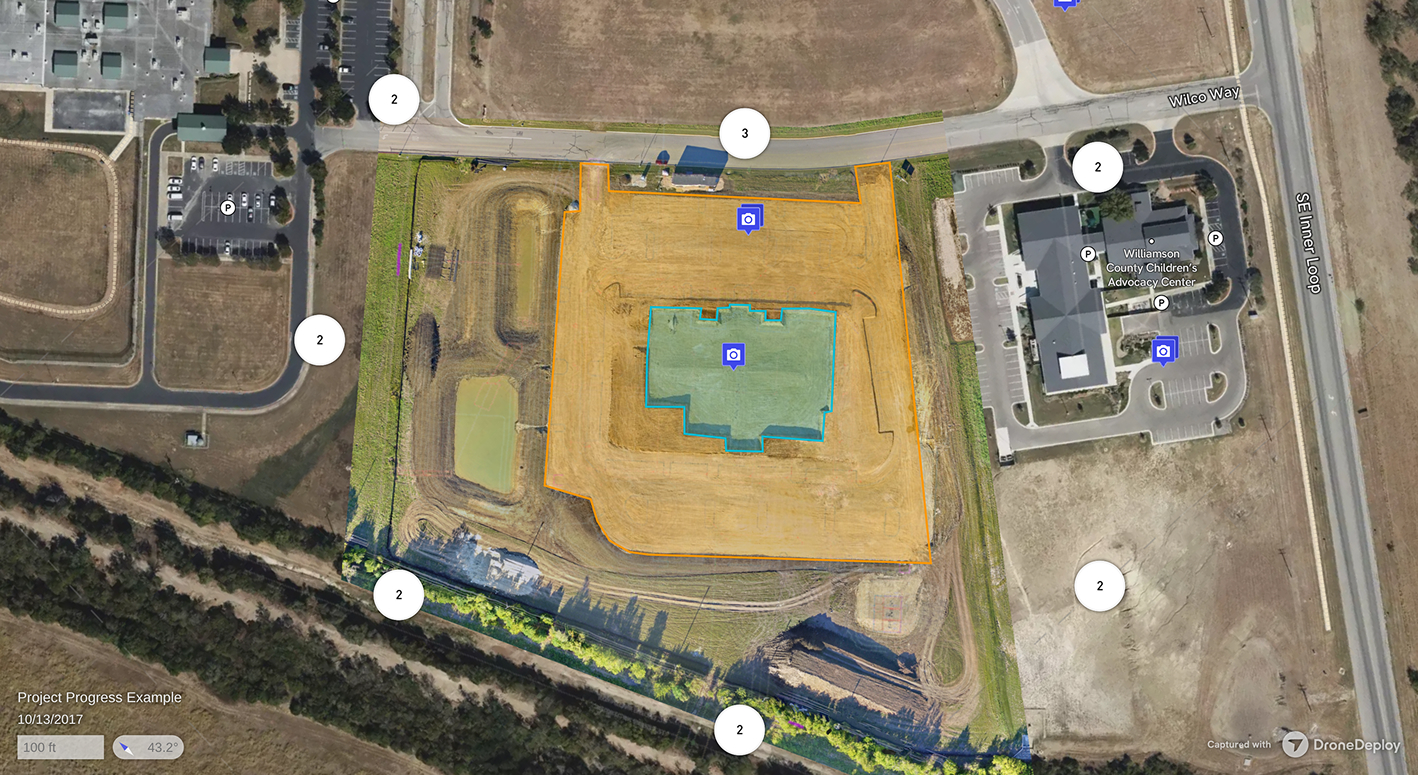 Aerial view of a construction site with cleared land and a building foundation, adjacent to the Williamson County Children's Advocacy Center and surrounding parking lots.