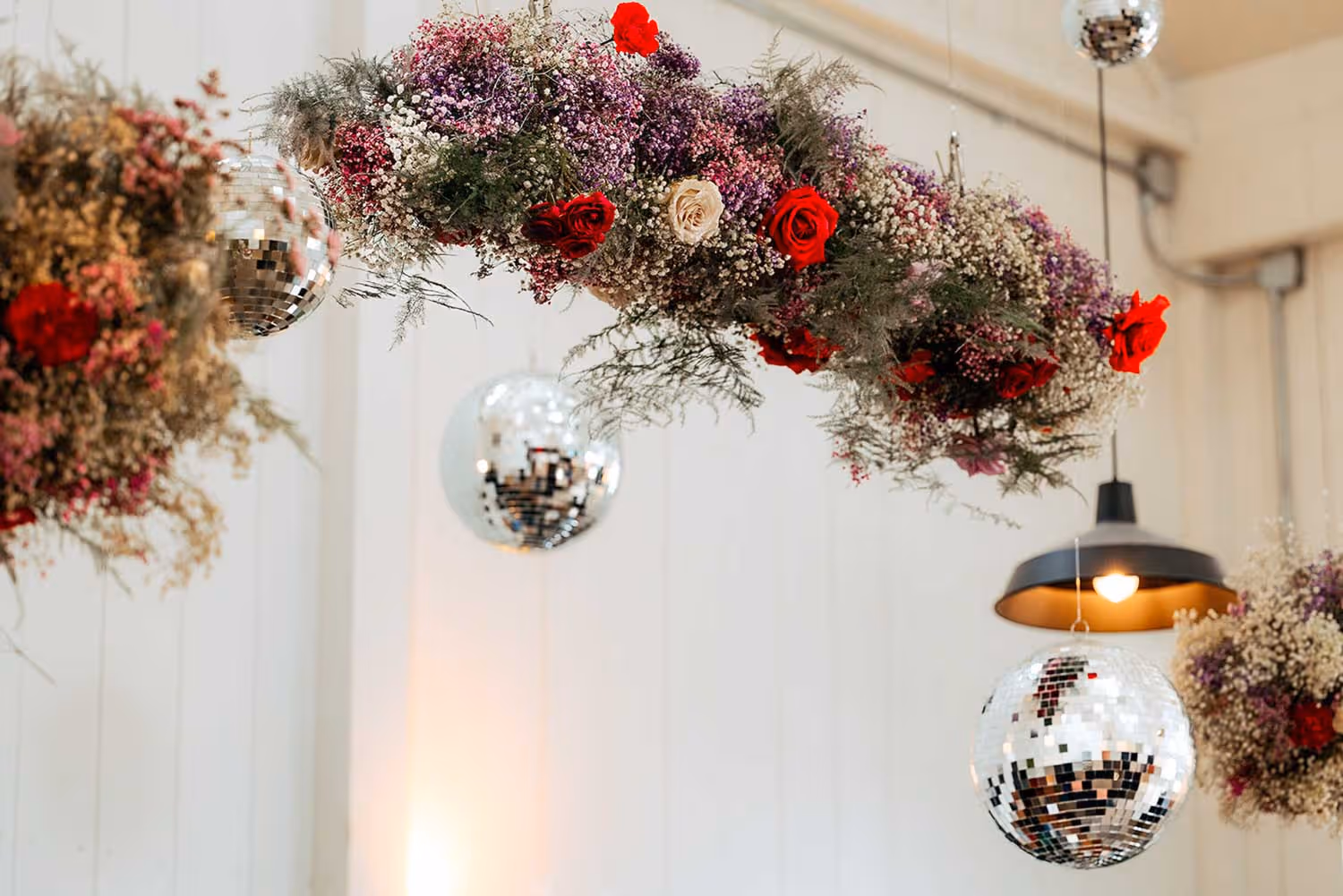 Hanging floral arrangement with red, white, and purple flowers alongside mirrored disco balls and ceiling lamp in a decorated interior.