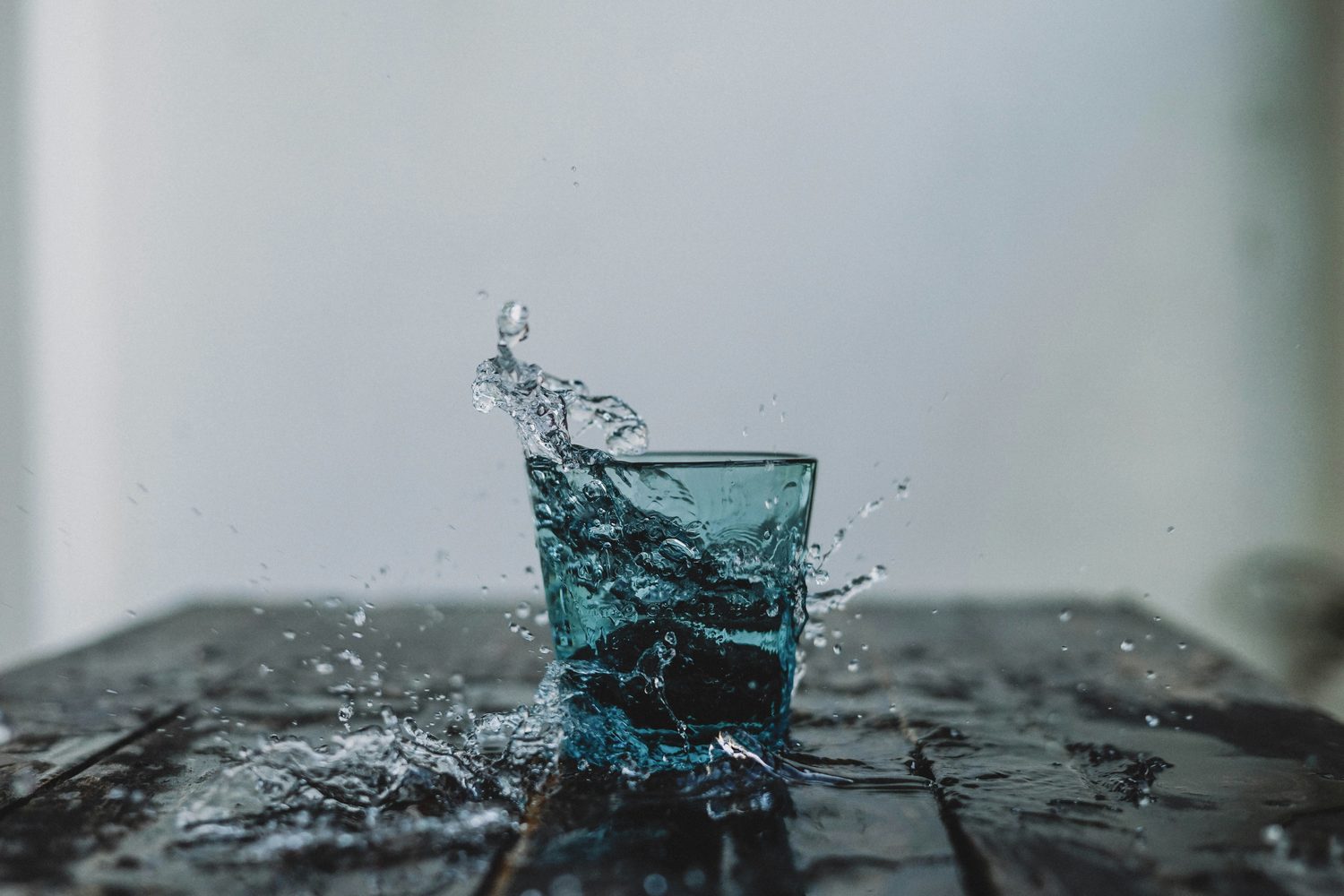 Water splashing out of a blue drinking glass on a wet wooden table