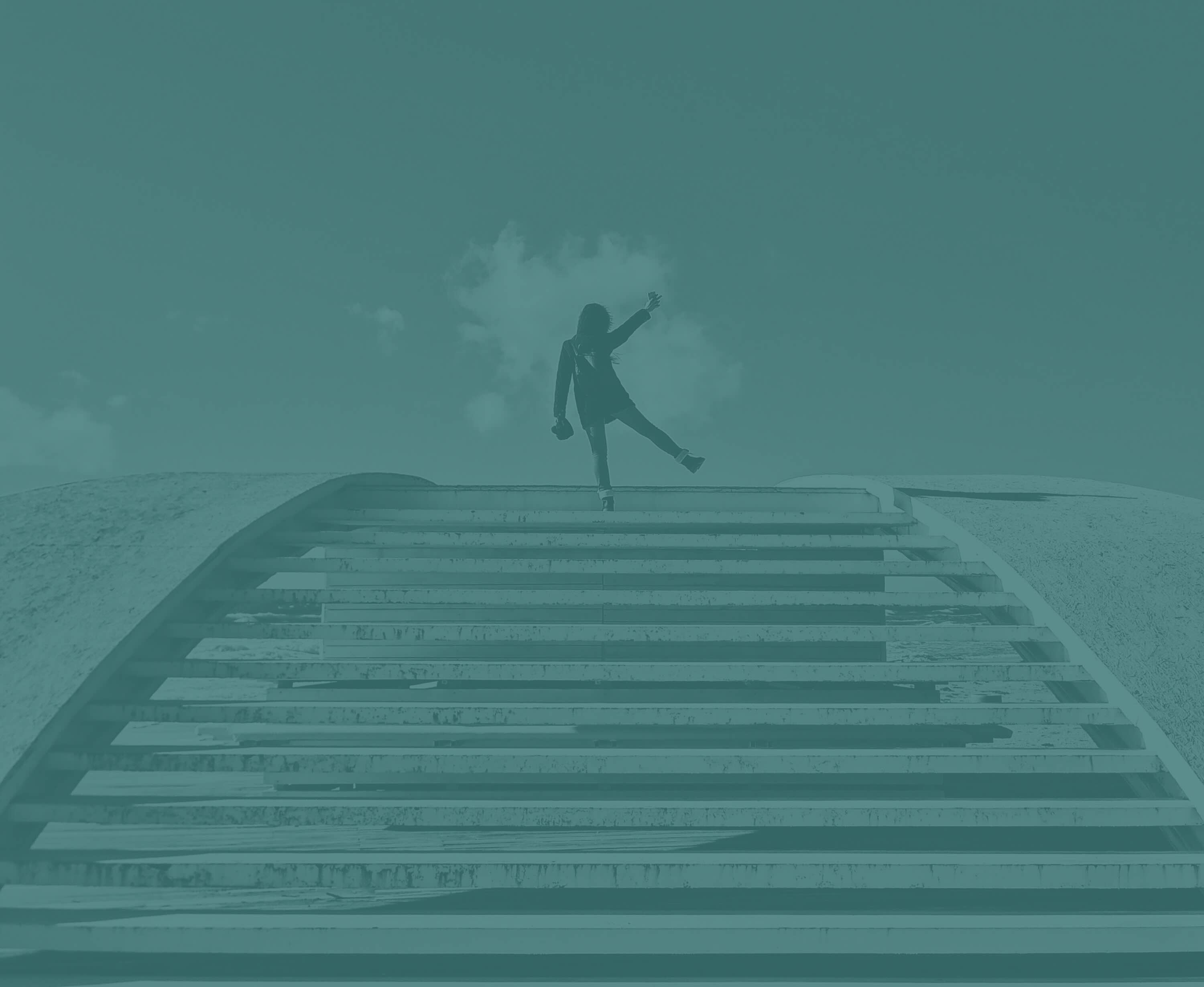 Person balancing on one leg atop wide, curved concrete steps under a partly cloudy sky.