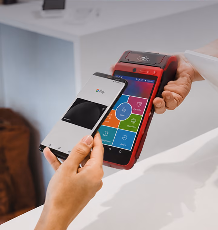 Person making a payment using smartphone with a small card reader held by another person at the counter.