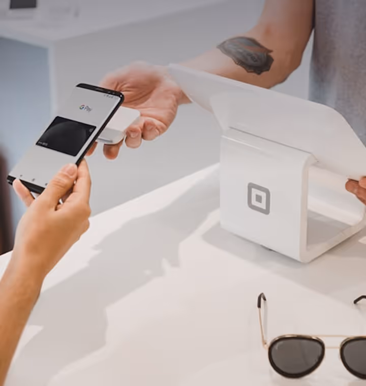 Person making a payment using smartphone with a small card reader held by another person at the counter.