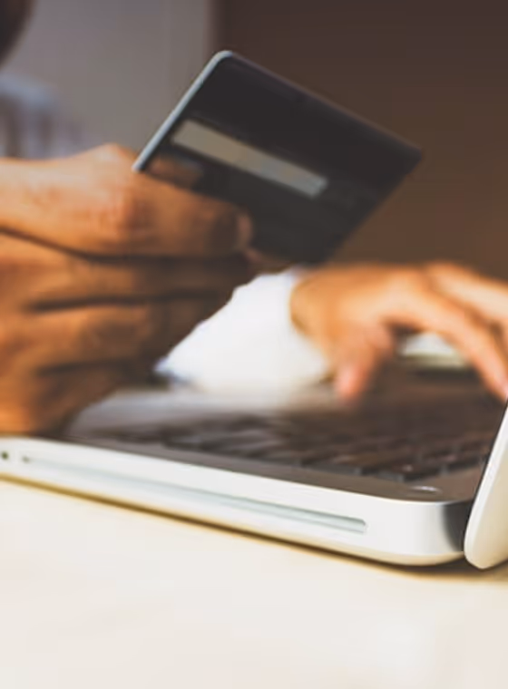 Person holding a credit card and typing on a laptop keyboard, suggesting online payment or shopping.