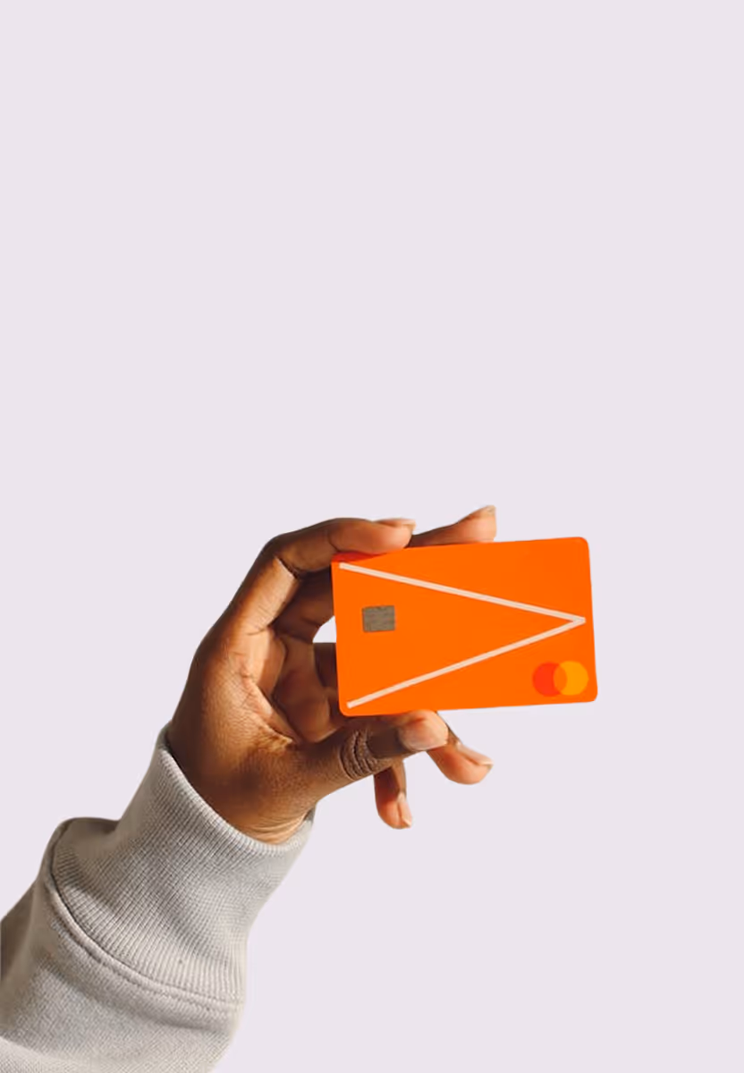 Hand holding an orange Mastercard credit card with white geometric lines on a white background.