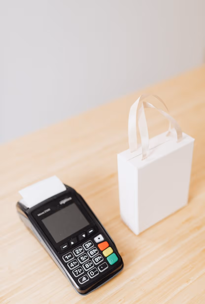 Black card payment terminal next to a small white paper shopping bag on a wooden surface.
