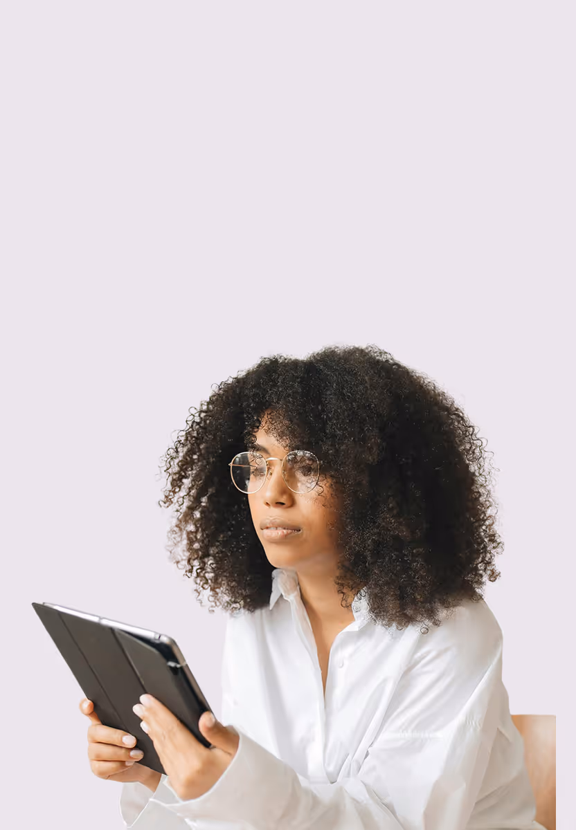Woman with curly hair and glasses wearing white shirt while holding and looking at a tablet.
