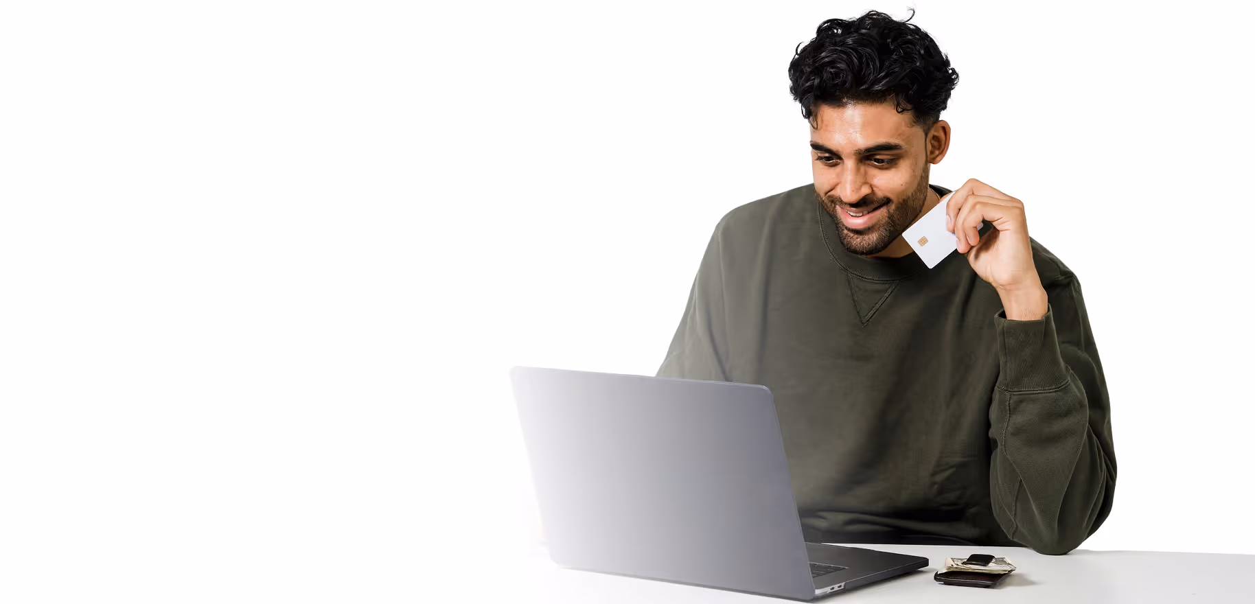 Man smiling while holding a credit card and using a laptop at a white table.