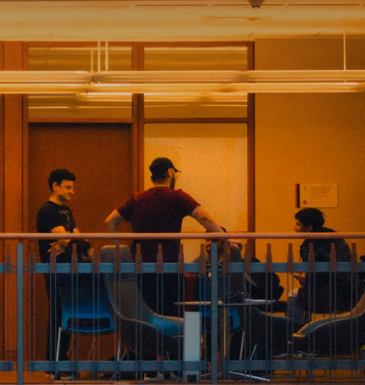 Group of people sitting and standing around tables having a discussion in a warmly lit indoor space.