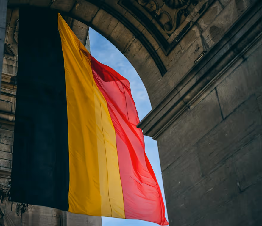 Large Belgian flag with black, yellow, and red stripes hanging under a stone archway.