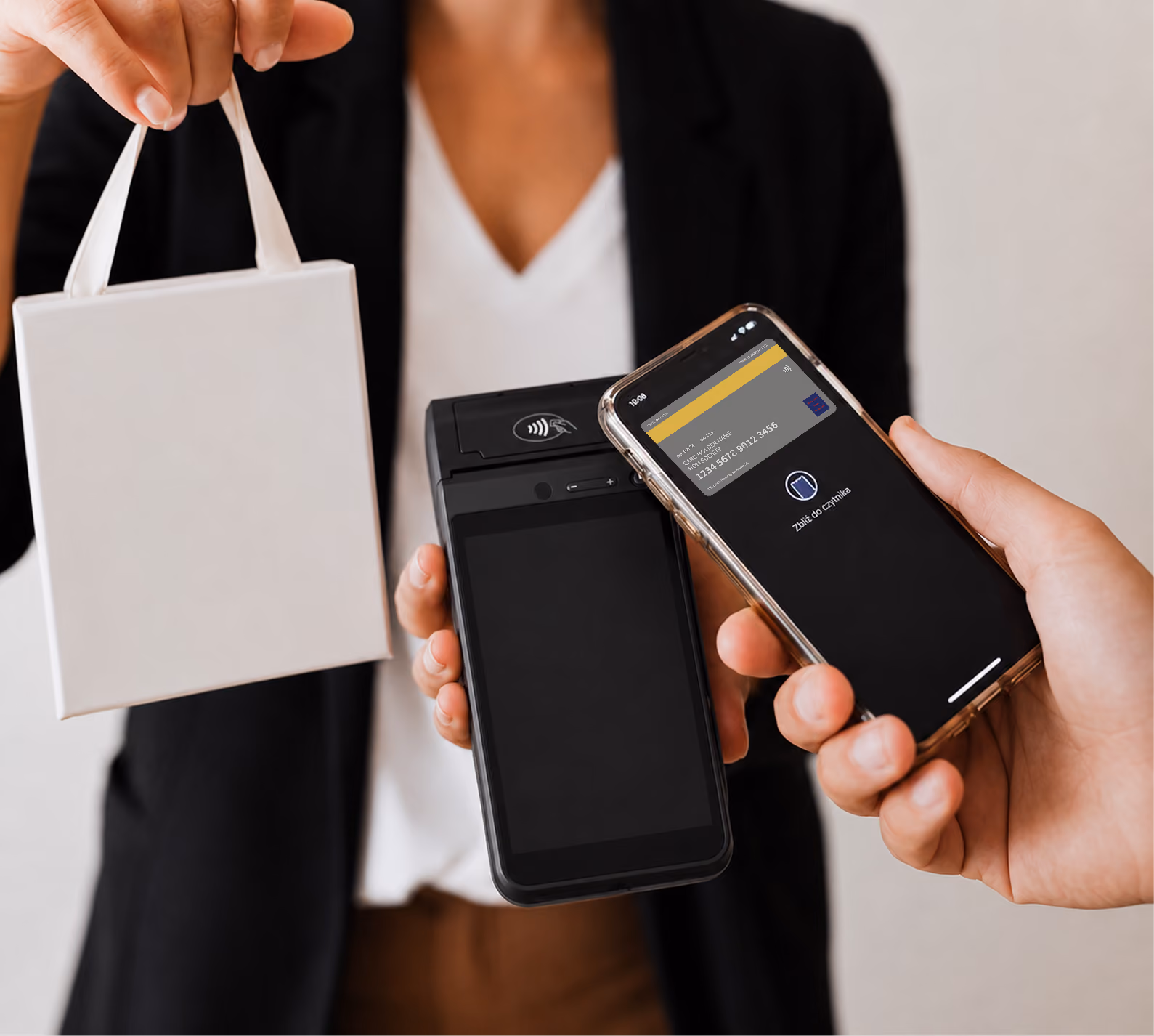 Person holding a white shopping bag and a card reader while another pays with a phone via contactless payment.