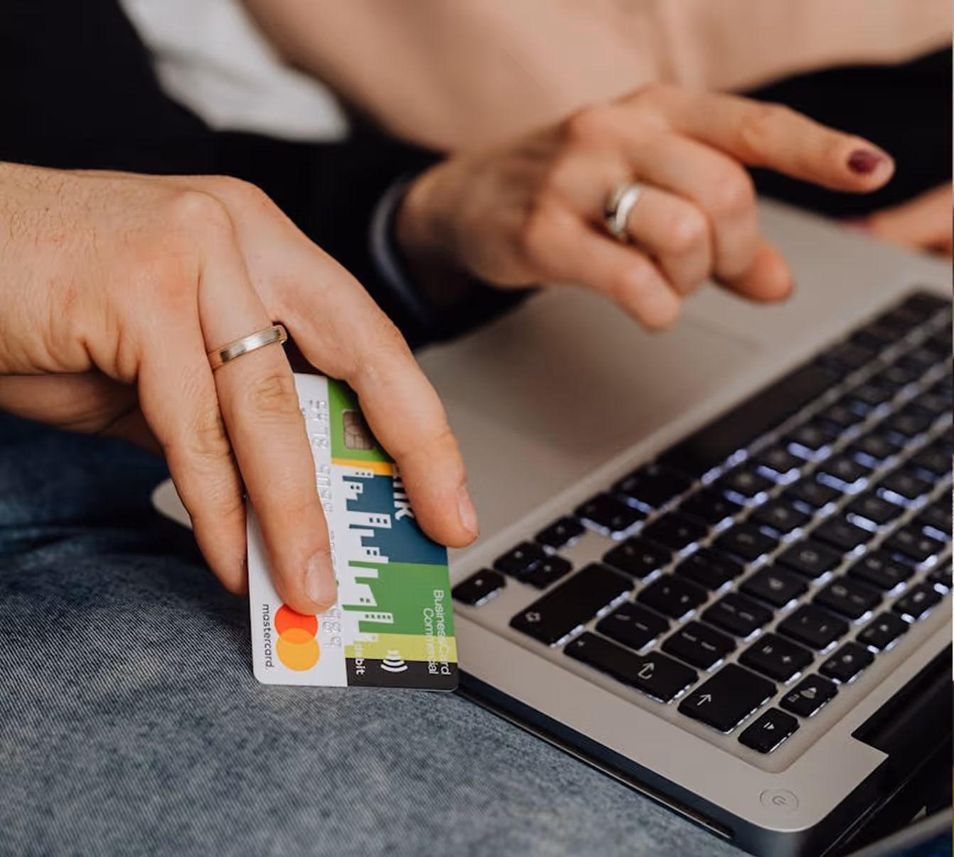 Hands holding a credit card and typing on a laptop keyboard for online payment.