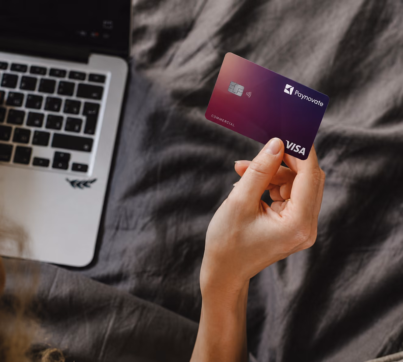 Person holding a yellow credit card near a laptop on a dark fabric surface.