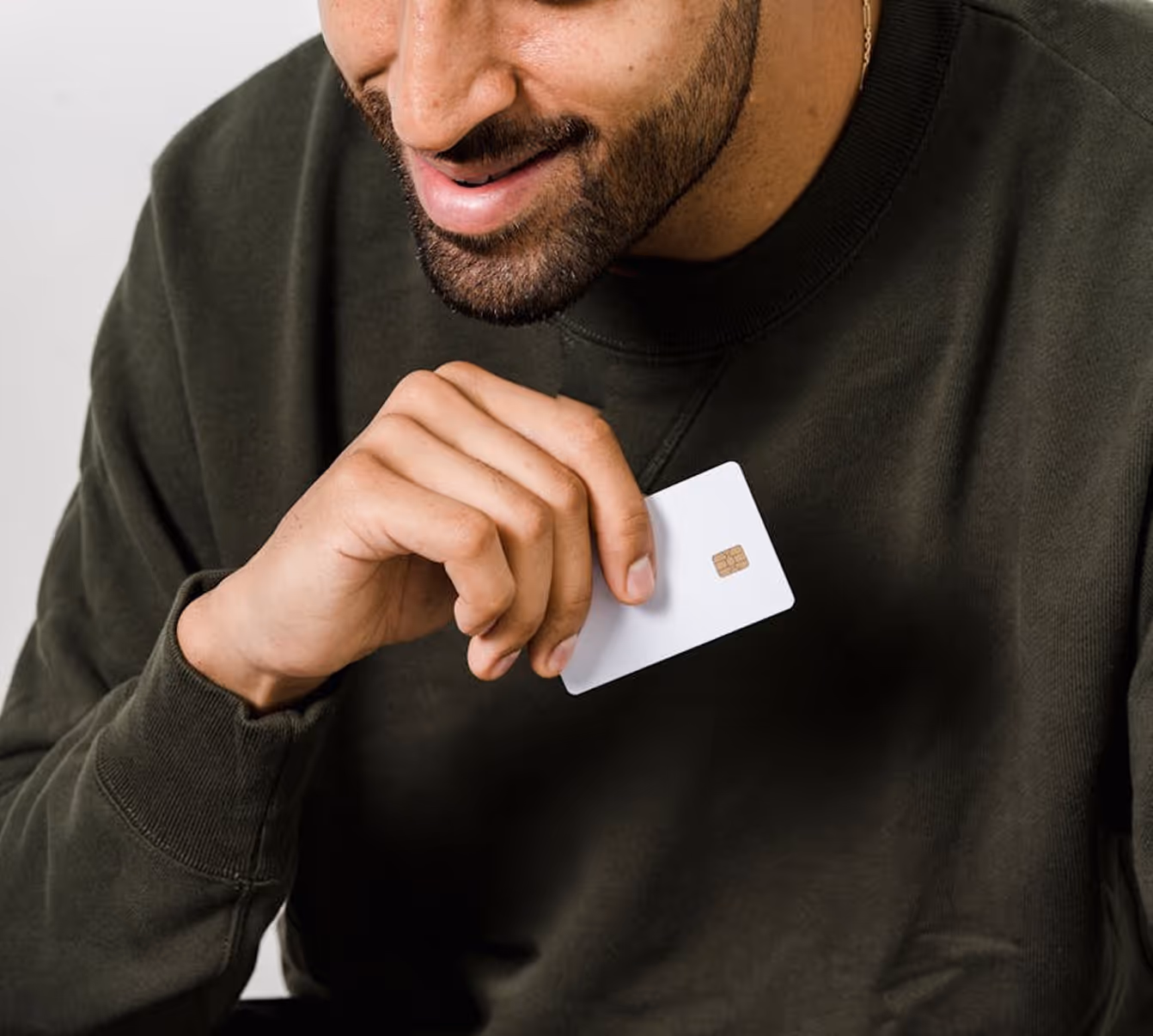Smiling man holding a blank white credit card with chip near his chest.