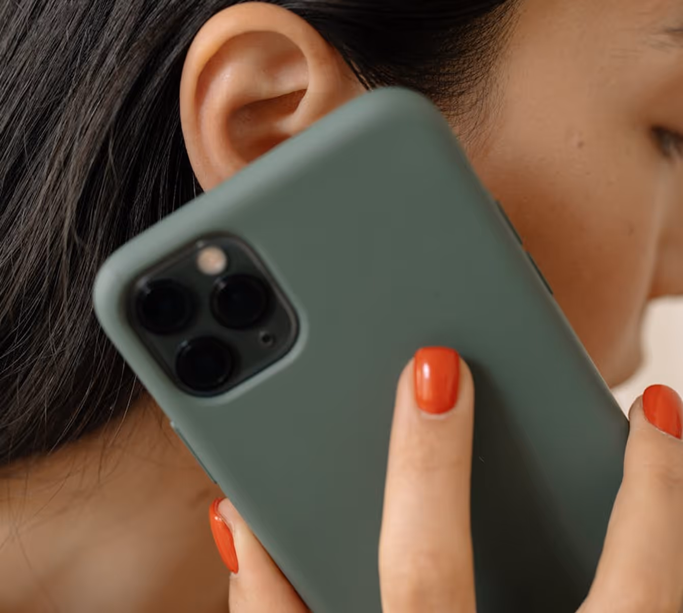 Close-up of a person holding a green phone with triple cameras near their ear.