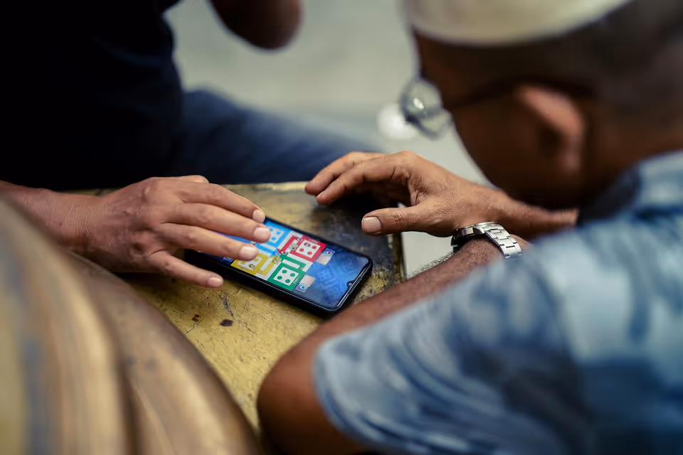 Two men sitting at a table playing a colorful game on a smartphone.
