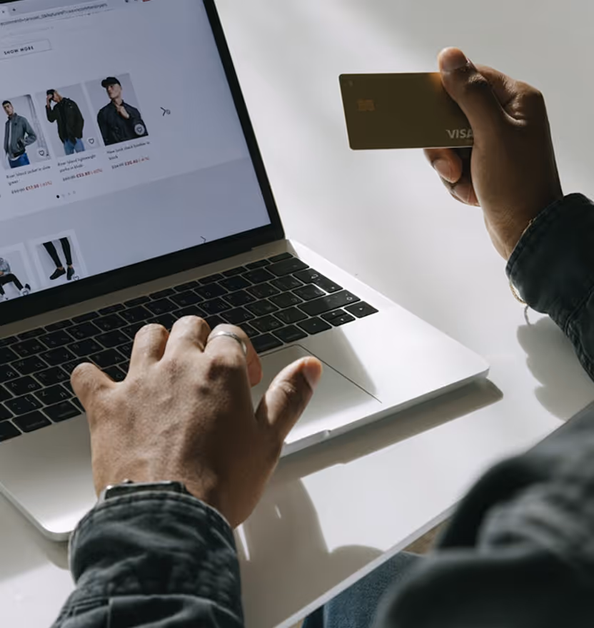 Person using a laptop to shop online while holding a Visa credit card in the other hand.