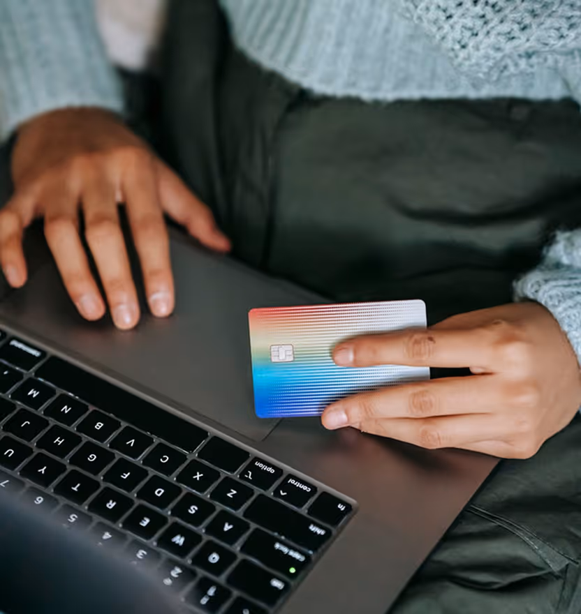 Person holding a colorful credit card above a laptop keyboard, preparing for online payment.