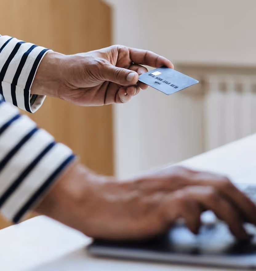 Person holding a credit card in one hand while using a laptop with the other hand.