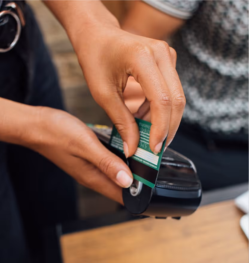 Person swiping a green credit card on a black card reader for payment.